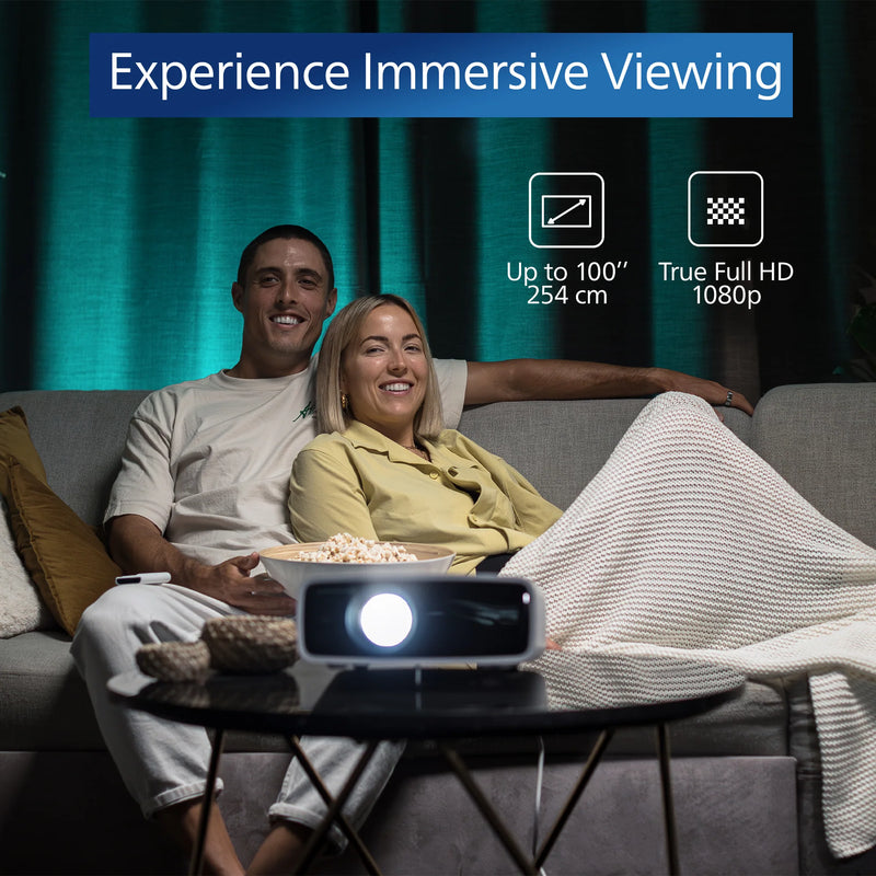 Man and woman sitting on a couch with a projector displaying 'Experience Immersive Viewing' text. Philips NeoPix 550 Smart Projector | White | Connec It Ireland